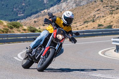 Yoldaki virajda motosikletini süren genç bir adam, ön planda güneşli bir günde fotoğraf. Fotoğraf Ağustos 2021 'de İspanya' nın Avila ilinde çekildi.