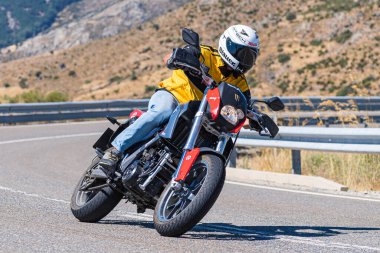 Yoldaki virajda motosikletini süren genç bir adam, ön planda güneşli bir günde fotoğraf. Fotoğraf Ağustos 2021 'de İspanya' nın Avila ilinde çekildi.