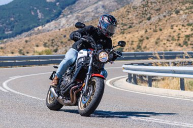 Yoldaki virajda motosikletini süren genç bir adam, ön planda güneşli bir günde fotoğraf. Fotoğraf Ağustos 2021 'de İspanya' nın Avila ilinde çekildi.