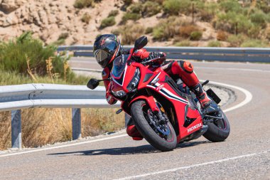 Yoldaki virajda motosikletini süren genç bir adam, ön planda güneşli bir günde fotoğraf. Fotoğraf Ağustos 2021 'de İspanya' nın Avila ilinde çekildi.