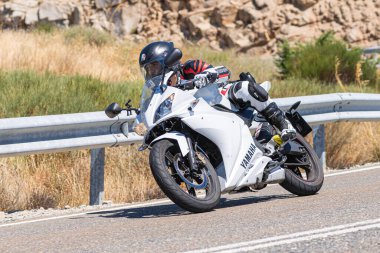 Yoldaki virajda motosikletini süren genç bir adam, ön planda güneşli bir günde fotoğraf. Fotoğraf Ağustos 2021 'de İspanya' nın Avila ilinde çekildi.