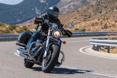 Yoldaki virajda motosikletini süren genç bir adam, ön planda güneşli bir günde fotoğraf. Fotoğraf Ağustos 2021 'de İspanya' nın Avila ilinde çekildi.