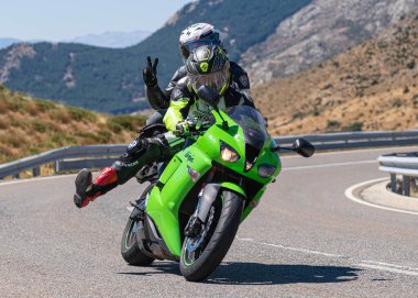 Yoldaki virajda motosikletini süren genç bir adam, ön planda güneşli bir günde fotoğraf. Fotoğraf Ağustos 2021 'de İspanya' nın Avila ilinde çekildi.