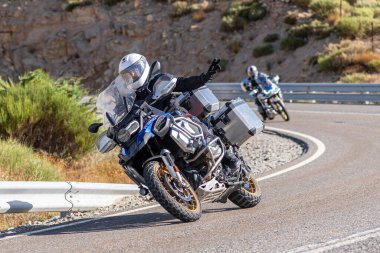 Yoldaki virajda motosikletini süren genç bir adam, ön planda güneşli bir günde fotoğraf. Fotoğraf Ağustos 2021 'de İspanya' nın Avila ilinde çekildi.