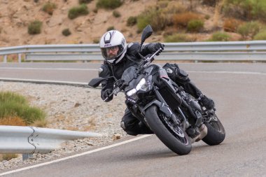 Yoldaki virajda motosikletini süren genç bir adam, ön planda güneşli bir günde fotoğraf. Fotoğraf Ağustos 2021 'de İspanya' nın Avila ilinde çekildi.