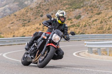 Yoldaki virajda motosikletini süren genç bir adam, ön planda güneşli bir günde fotoğraf. Fotoğraf Ağustos 2021 'de İspanya' nın Avila ilinde çekildi.