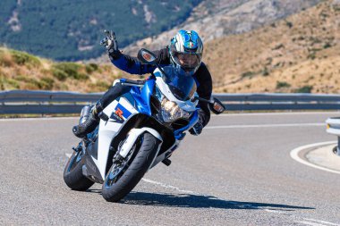 Motorcu, Avila limanında bir viraj alıyor güneşli bir gün ve dağ gibi bir geçmişi var. Fotoğraf 29 Ağustos 2020 'de Navalmoral de la Sierra, Avila, İspanya' da çekildi.