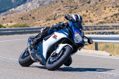 Motorcu, Avila limanında bir viraj alıyor güneşli bir gün ve dağ gibi bir geçmişi var. Fotoğraf 29 Ağustos 2020 'de Navalmoral de la Sierra, Avila, İspanya' da çekildi.