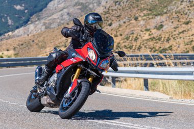 Makinesinde motosikletli, keskin bir virajda yolda seyahat ediyor. Fotoğraf: Navalmoral de la Sierra-Avila, İspanya 'da Ağustos 2022' de çekilmiştir..