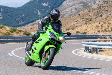 Makinesinde motosikletli, keskin bir virajda yolda seyahat ediyor. Fotoğraf: Navalmoral de la Sierra-Avila, İspanya 'da Ağustos 2022' de çekilmiştir..