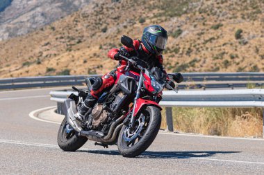 Makinesinde motosikletli, keskin bir virajda yolda seyahat ediyor. Fotoğraf: Navalmoral de la Sierra-Avila, İspanya 'da Ağustos 2022' de çekilmiştir..
