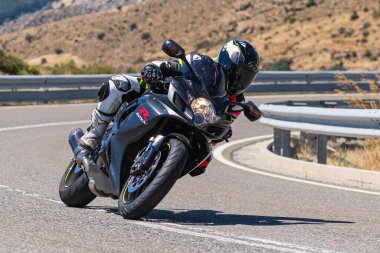 Makinesinde motosikletli, keskin bir virajda yolda seyahat ediyor. Fotoğraf: Navalmoral de la Sierra-Avila, İspanya 'da Ağustos 2022' de çekilmiştir..