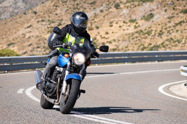 Makinesinde motosikletli, keskin bir virajda yolda seyahat ediyor. Fotoğraf: Navalmoral de la Sierra-Avila, İspanya 'da Ağustos 2022' de çekilmiştir..
