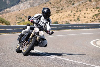 Makinesinde motosikletli, keskin bir virajda yolda seyahat ediyor. Fotoğraf: Navalmoral de la Sierra-Avila, İspanya 'da Ağustos 2022' de çekilmiştir..