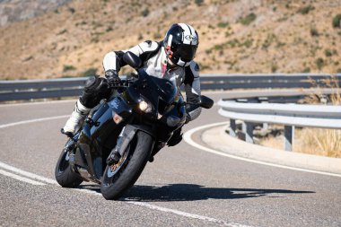 Makinesinde motosikletli, keskin bir virajda yolda seyahat ediyor. Fotoğraf: Navalmoral de la Sierra-Avila, İspanya 'da Ağustos 2022' de çekilmiştir..