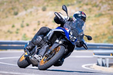 Motorcu güneşli bir günde yolda keskin bir viraj alıyor. Fotoğraf 12 Ağustos 2023 'te İspanya' nın Avila kentindeki Navalmoral de la Sierra kasabasında çekildi..