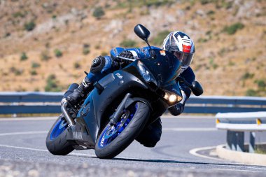 Motorcu güneşli bir günde yolda keskin bir viraj alıyor. Fotoğraf 12 Ağustos 2023 'te İspanya' nın Avila kentindeki Navalmoral de la Sierra kasabasında çekildi..