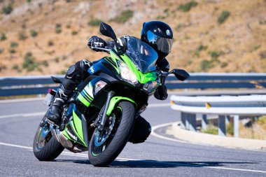 Motorcu güneşli bir günde yolda keskin bir viraj alıyor. Fotoğraf 12 Ağustos 2023 'te İspanya' nın Avila kentindeki Navalmoral de la Sierra kasabasında çekildi..