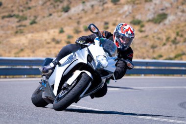 Motorcu güneşli bir günde yolda keskin bir viraj alıyor. Fotoğraf 12 Ağustos 2023 'te İspanya' nın Avila kentindeki Navalmoral de la Sierra kasabasında çekildi..