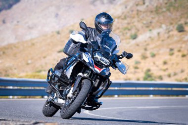 Motorcu güneşli bir günde yolda keskin bir viraj alıyor. Fotoğraf 12 Ağustos 2023 'te İspanya' nın Avila kentindeki Navalmoral de la Sierra kasabasında çekildi..