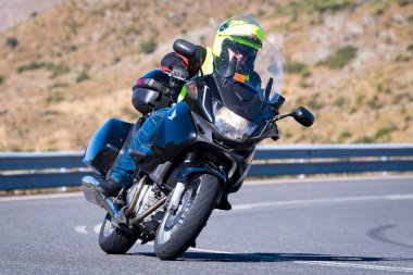 Motorcu güneşli bir günde yolda keskin bir viraj alıyor. Fotoğraf 12 Ağustos 2023 'te İspanya' nın Avila kentindeki Navalmoral de la Sierra kasabasında çekildi..
