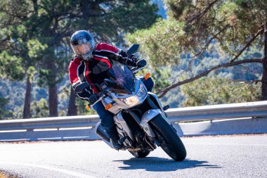 Motosikletinde oturan bir adam yolda oturmuş manzaranın ve güneşli günün tadını çıkarıyordu. Fotoğraf Mayıs 2024 'te Navaluenga kasabasında çekildi (Avila, İspanya).