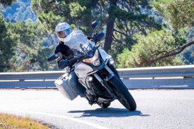 Motosikletinde oturan bir adam yolda oturmuş manzaranın ve güneşli günün tadını çıkarıyordu. Fotoğraf Mayıs 2024 'te Navaluenga kasabasında çekildi (Avila, İspanya).