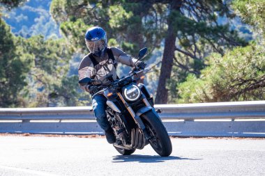 Motosikletinde oturan bir adam yolda oturmuş manzaranın ve güneşli günün tadını çıkarıyordu. Fotoğraf Mayıs 2024 'te Navaluenga kasabasında çekildi (Avila, İspanya).