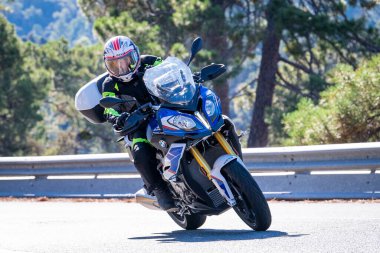 Motosikletinde oturan bir adam yolda oturmuş manzaranın ve güneşli günün tadını çıkarıyordu. Fotoğraf Mayıs 2024 'te Navaluenga kasabasında çekildi (Avila, İspanya).
