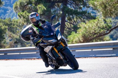 Motosikletinde oturan bir adam yolda oturmuş manzaranın ve güneşli günün tadını çıkarıyordu. Fotoğraf Mayıs 2024 'te Navaluenga kasabasında çekildi (Avila, İspanya).