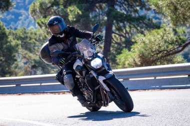 Motosikletinde oturan bir adam yolda oturmuş manzaranın ve güneşli günün tadını çıkarıyordu. Fotoğraf Mayıs 2024 'te Navaluenga kasabasında çekildi (Avila, İspanya).