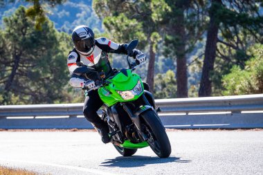 Motosikletinde oturan bir adam yolda oturmuş manzaranın ve güneşli günün tadını çıkarıyordu. Fotoğraf Mayıs 2024 'te Navaluenga kasabasında çekildi (Avila, İspanya).