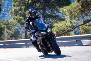 Motosikletinde oturan bir adam yolda oturmuş manzaranın ve güneşli günün tadını çıkarıyordu. Fotoğraf Mayıs 2024 'te Navaluenga kasabasında çekildi (Avila, İspanya).