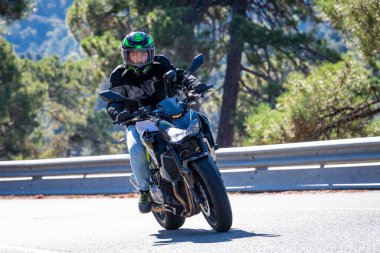 Motosikletinde oturan bir adam yolda oturmuş manzaranın ve güneşli günün tadını çıkarıyordu. Fotoğraf Mayıs 2024 'te Navaluenga kasabasında çekildi (Avila, İspanya).