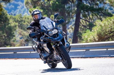 Motosikletinde oturan bir adam yolda oturmuş manzaranın ve güneşli günün tadını çıkarıyordu. Fotoğraf Mayıs 2024 'te Navaluenga kasabasında çekildi (Avila, İspanya).