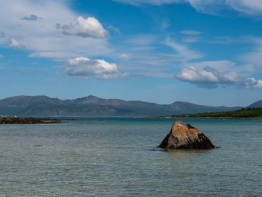 Uzaktaki dağlarla mavi sularda sarkan bir kaya.