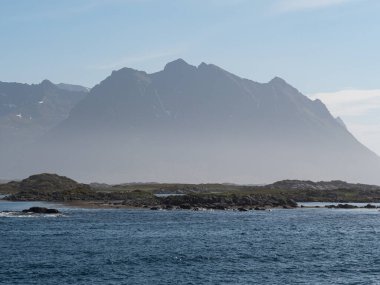 Önünde deniz olan sisli bir dağ.