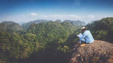 Asian man travel relax in the holiday. seats relax read books on rocky cliffs. On the Moutain. In Thailand clipart