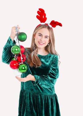 Geyik geyiği boynuzu takan, Noel süsleri taşıyan, izole edilmiş beyaz arka planda güzel giyinmiş bir kız. Noel konsepti