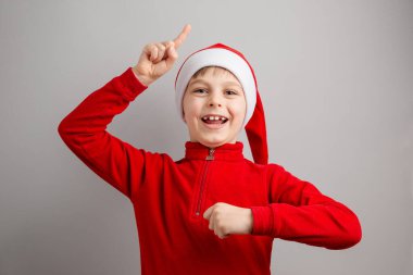 Noel Baba şapkalı neşeli çocuk izole edilmiş gri arka planda farklı duygular gösteriyor, sürpriz, neşe, keyif. Mutlu Noeller..