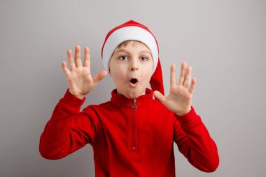 Noel Baba şapkalı neşeli çocuk izole edilmiş gri arka planda farklı duygular gösteriyor, sürpriz, neşe, keyif. Mutlu Noeller..