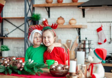 Erkek ve kız kardeş, küçük oğlan ve kız Noel kurabiyesi yiyor ve mutfakta Noel süslemelerinde içki içiyorlar. Kış tatili. Noel