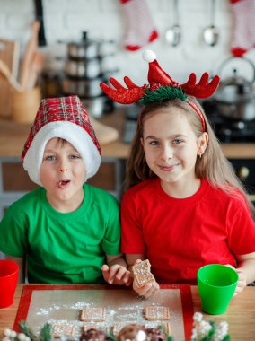 Erkek ve kız kardeş, küçük oğlan ve kız Noel kurabiyesi yiyor ve mutfakta Noel süslemelerinde içki içiyorlar. Kış tatili. Noel