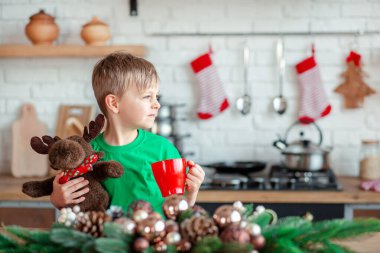 Sevimli küçük çocuk Noel kurabiyesi yiyor ve mutfakta Noel süslemelerinde içki içiyor. Kış tatili. Noel