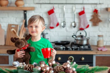 Sevimli küçük çocuk Noel kurabiyesi yiyor ve mutfakta Noel süslemelerinde içki içiyor. Kış tatili. Noel