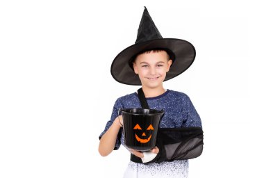 Cadılar Bayramı konsepti. Siyah cadı şapkalı, yaralı elli, tatlı şekerlemeler için kova kabaklı duygusal çocuk portresi. İzole edilmiş beyaz arkaplan