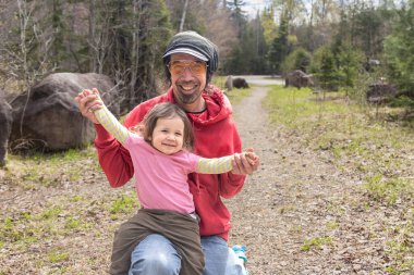 Babası, genç kızını kollarında tutarken bir yolda diz çöküyor. Kız sevinçle kollarını uzatıyor.