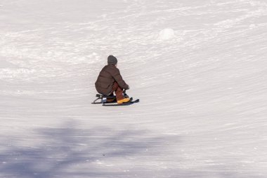 Kicksled tepesinde kayak yapan, çocukluk özgürlüğü ve kış tatili somutlaştıran adam neşeyle kızaktan kayıyor. Seçici odak