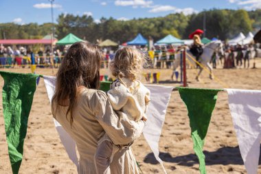 Anne kucağında küçük oğlunu bir ortaçağ festivalinde mızrak dövüşü turnuvasıyla izliyor.