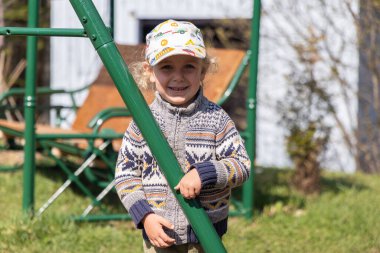 Gülümseyen ve elinde beyzbol şapkası ve süveteri olan yeşil maymun parmaklıklarına tutunan genç bir çocuk. Seçici odak